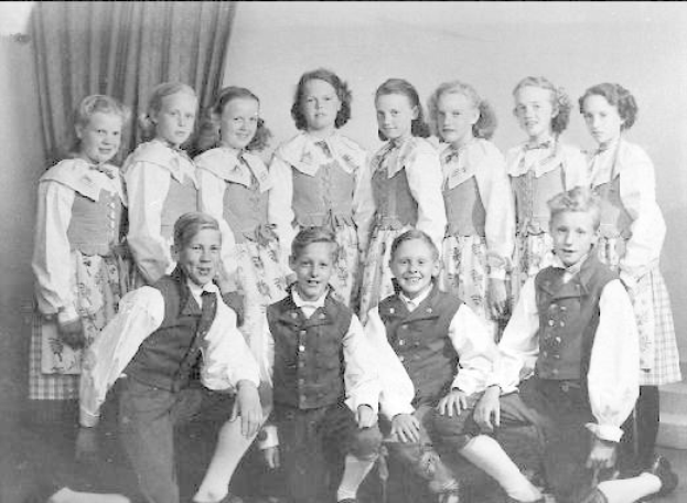 Ein Schwarz-Weiß-Foto einer Gruppe von Kindern, die vor einer Wand mit einem Vorhang posieren, mit dem Text "1930er Kinder-Schule" unten.
