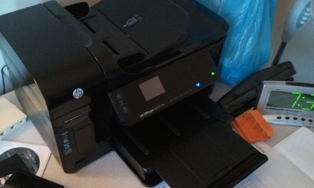Ein digitaler Timer, ein HP-Drucker, eine blaue Polyethylenabdeckung, eine CD in ihrer Hülle, Papier und einige andere Gegenstände sind auf einem Tisch angeordnet.