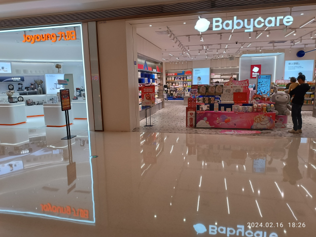Babycare-Laden im Innern des Mall of Asia mit Regalen voller Produkte, Schildern, einem Display, Deckenleuchten und einer Gruppe von Menschen umgeben von Spielzeugen.