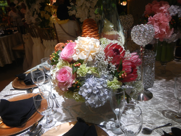 Formal dinner table setting with plates, cutlery, glasses, napkins, and a floral centerpiece, surrounded by chairs and occupied tables in the background.