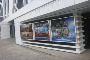 Großes Plakat an einem Gebäude, das die Eröffnungszeremonie der Olympischen Spiele in Moskau ankündigt, mit sichtbarer Boden- und Rechtsbeleuchtung.