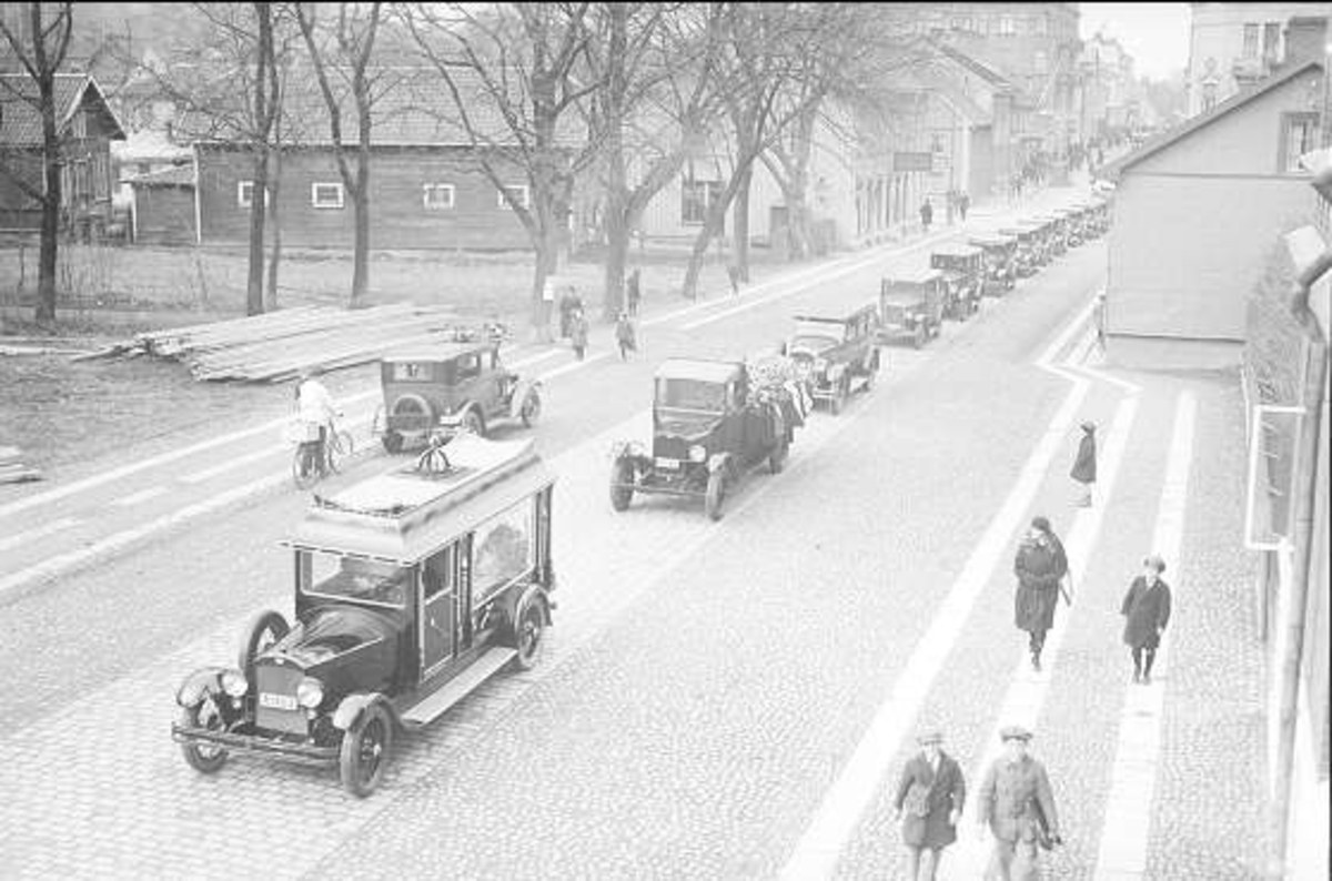 Schwarze und weiße Straßenszene in den 1930er bis 1940er Jahren in Berlin mit parkenden Autos, Fußgängern, Gebäuden, Bäumen und einem klaren Himmel, mit dem Text "1930-1940er Jahre deutsche Autos in Berlin" unten.