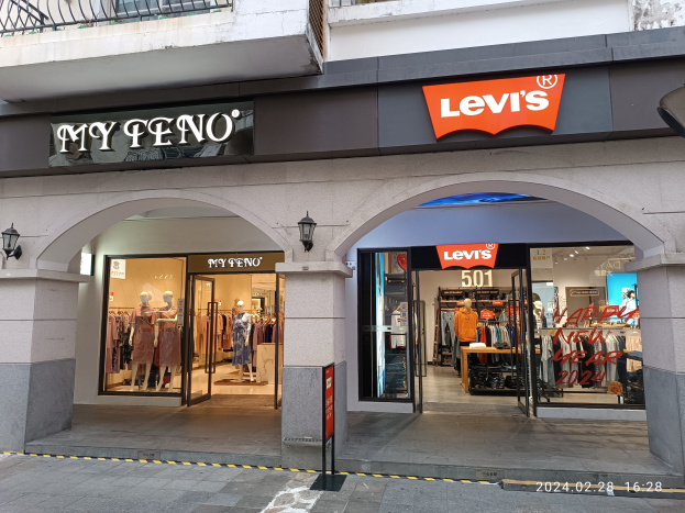 Ladenfront von Levi's mit Schaufensterpuppen in Kleidern, hängenden Kleidern und beleuchteten Schildern über einer Straße.