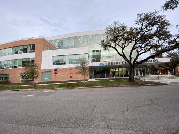 Presbyte Mittelschule, ein großes Gebäude mit zahlreichen Fenstern, umgeben von Bäumen, Gras, Schildern, Pfosten und einer Straße, mit einem bewölkten Himmel im Hintergrund.