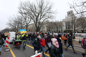 Eine große Gruppe von Menschen nimmt an einer Protestdemo in Washington, D.C. teil, sie halten Plakate und Banner und einige fahren Fahrräder, mit Bäumen und Schildern gegen einen klaren blauen Himmel.