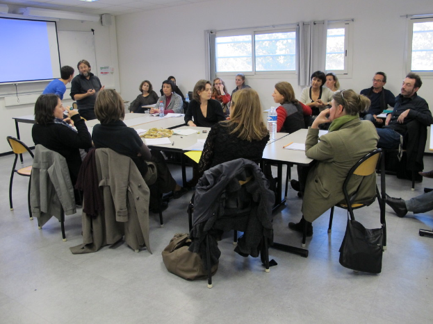 Eine Gruppe von Menschen, die sich unterhält und diskutiert, wobei zwei Personen im Hintergrund stehen und miteinander sprechen.