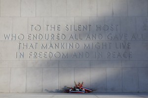 Eine Gedenkwand mit einer Inschrift, die stille Gastgeber ehrt, umgeben von einem Blumenstrauß.