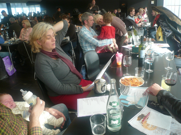 Einblicke in ein volles Restaurant mit Gästen an Tischen, die Gläser, Teller mit Essen, Getränkeflaschen, Speisekarten und andere Gegenstände haben.
