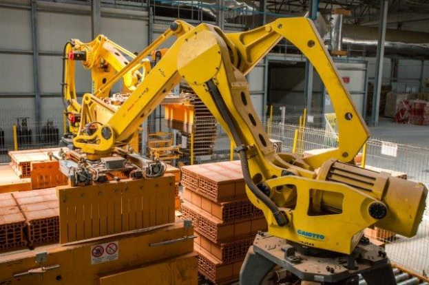 Großes Industriehochregallager mit gestapelten Kisten, Kranbrücken, Zaun, Pfählen und einer fernen Wand in einer automatisierten Fertigungsumgebung.