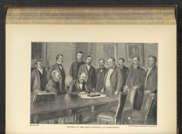 Eine Gruppe von Männern steht um einen Tisch mit Papieren und Gegenständen, ein Mann sitzt in der Mitte, mit Fotorahmen an der Wand im Hintergrund und Text unten, der 'Unterzeichnung des Friedensprotokolls in Washington' lautet.