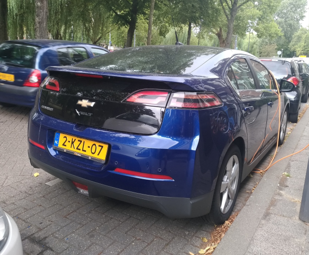 Elektroauto an einer Ladestation auf einer baumgesäumten Straße unter einem klaren blauen Himmel