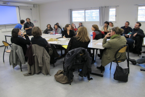 Eine Gruppe von Menschen, die sich unterhält und diskutiert, wobei zwei Personen im Hintergrund stehen und miteinander sprechen.