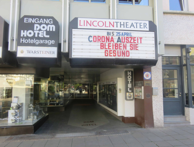 Außenansicht des Lincoln Theaters in Berlin, Deutschland, mit Glasfenstern und -türen sowie einer Schautafel und einem Inneren, das eine belebte Stadtatmosphäre suggeriert.