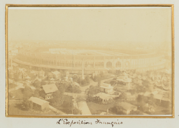 Altes Schwarz-Weiß-Foto eines Stadions umgeben von Gebäuden, Bäumen und Strommasten mit Text unten.