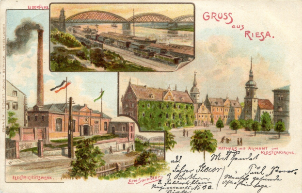 Alte Ansichtskarte zeigt eine Stadtlandschaft mit Gebäuden, Bäumen, Strommasten, Fahnen, einer Brücke, einem rauchenden Zug auf Schienen und einem Himmel, mit handschriftlichem Text auf der Vorderseite.