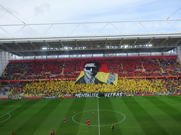 Ein Fußballstadion voller Menschen auf dem Feld und in den Rängen, mit einem zentralen Banner mit einem Porträt und Text, Heimstadion des Watford Football Club.