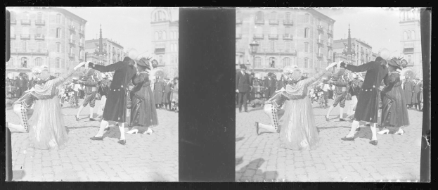 Ein Schwarz-Weiß-Foto einer Gruppe von Menschen, die auf der Straße tanzen, umgeben von Gebäuden, Straßenlaternen und einer klaren Nacht.