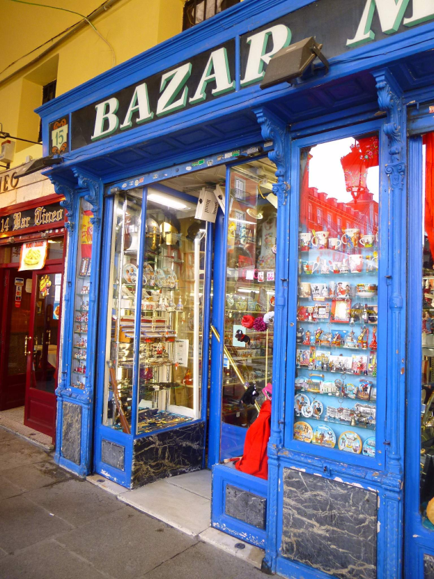 Ein Ladengeschäft mit einer blauen Tür und einem Schild mit der Aufschrift "Bazar", das verschiedene Gegenstände in Schränken zeigt.