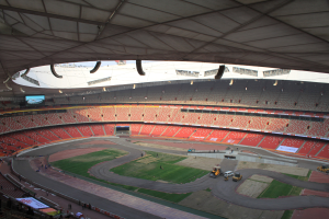 Großes Stadion voller Zuschauer, Fahrzeuge auf der Straße, Rasenfläche, Texttafeln, Geländer, ein Bildschirm und Deckenbeleuchtung.