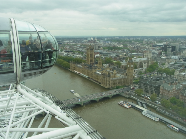 Luftaufnahme des Parlamentsgebäudes in London, das eine Brücke, zahlreiche Gebäude und einen bewölkten Himmel zeigt.