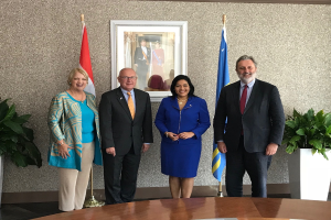 Eine Gruppe strahlender Menschen steht um einen Tisch mit Papieren herum, umgeben von Fahnen, Topfpflanzen und einem Foto auf der Wand, feiert die Unterzeichnung eines Memorandums zwischen den Vereinigten Staaten und Kanada.