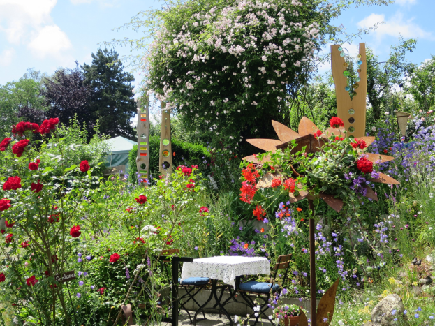 Ein Garten mit bunten Blumen und Pflanzen, der einen Tisch mit einer Decke und Stühlen zeigt, vor Bäumen und einem bewölkten Himmel bei der Chelsea Flower Show.