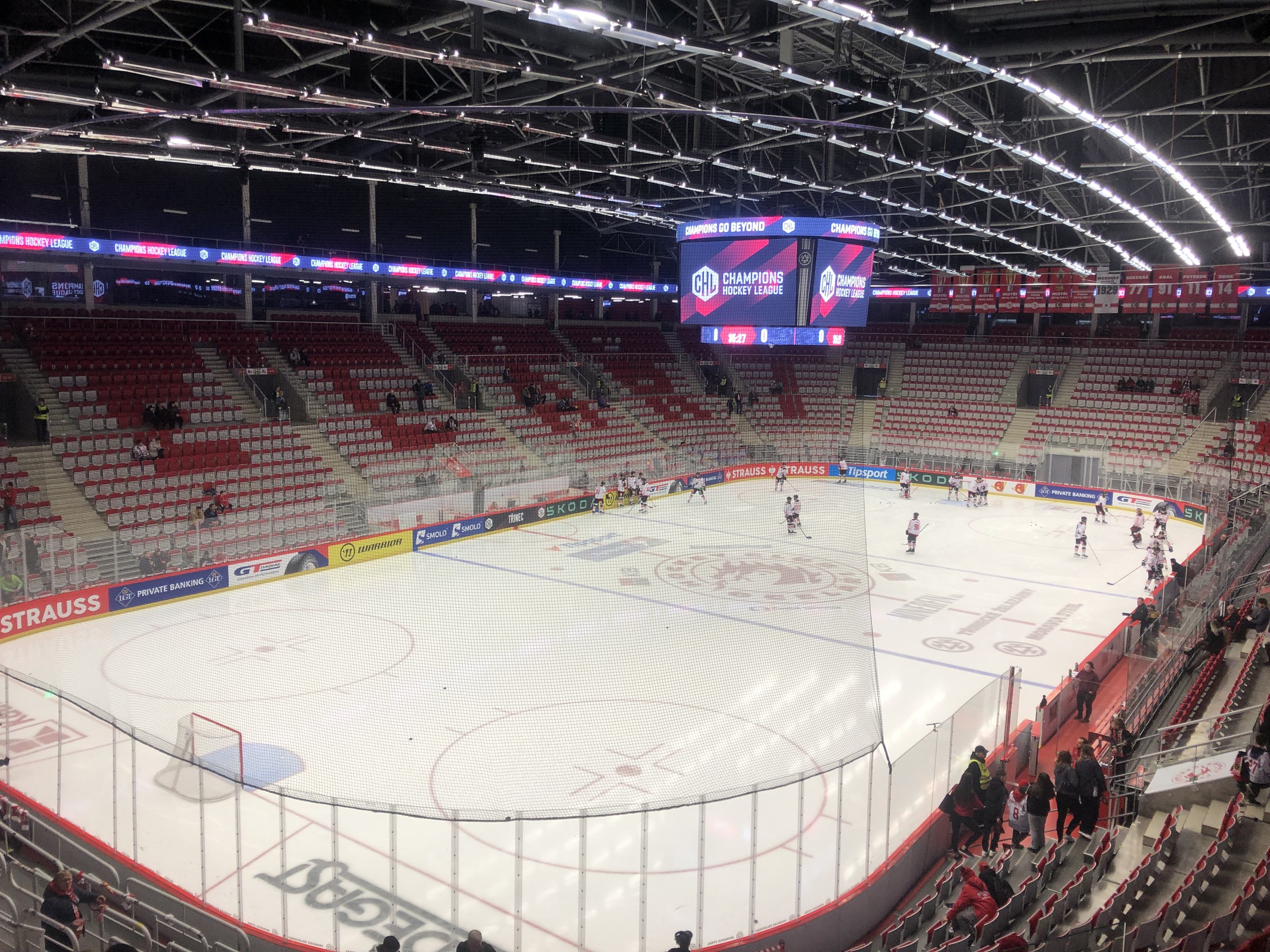 Eishockeyspiel in einer großen Arena mit Zuschauern, ein von einem Zaun umgebenes Feld, ein Display, das "St. Louis Blues vs Detroit Red Wings" anzeigt, und Deckenbeleuchtung.
