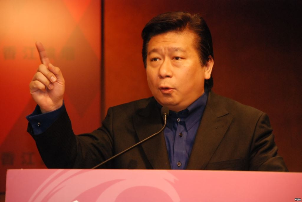 Ein Mann im Anzug und mit Krawatte, der eine Rede an einem Rednerpult mit Mikrofon hält und wie ein Politologe mit ernster Miene wirkt.