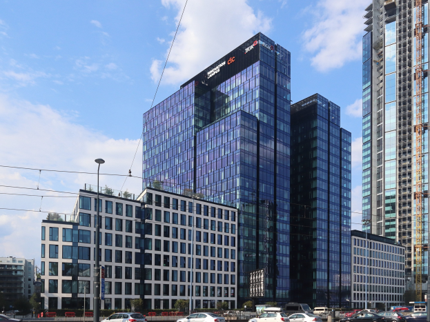 Ein großes Hauptgebäude der Deutschen Bank in Frankfurt, Deutschland, umgeben von städtischer Infrastruktur wie Straßenlaternen, Lichtern, Fahrzeugen, Grünflächen und einem bewölkten Himmel.