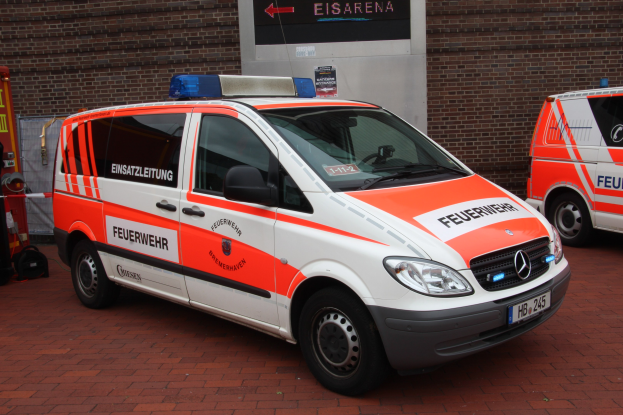 Zwei weiße Rettungswagen nebeneinander vor einem Gebäude mit einer Wand im Hintergrund geparkt, mit einem Feuerlöscher auf der linken Seite.