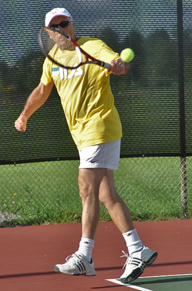 Ein Mann mit Brille, T-Shirt, Baseballkappe und Schuhen spielt Tennis.