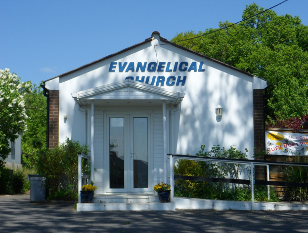 Evangelische Kirche mit Straße im Vordergrund, Grünfläche im Hintergrund und einem klaren blauen Himmel.