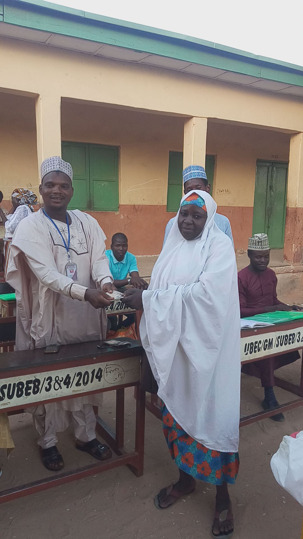 Eine Gruppe von Menschen steht und sitzt um einen Tisch mit Papieren und Gegenständen, die bei einer Wahlurne abstimmen.