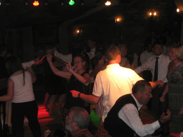 Eine lebendige Partyszene mit tanzenden Menschen unter verschiedenen bunten Lichtern in einem dunklen Raum.