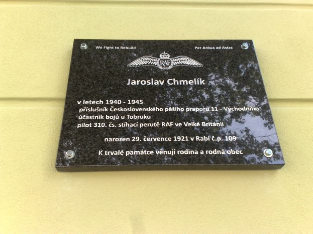 Eine schwarze Plakette mit weißer Schrift, die "Jaroslav Chmelik" lautet und einen dekorativen Rahmen hat, die an einer Gebäudewand angebracht ist.