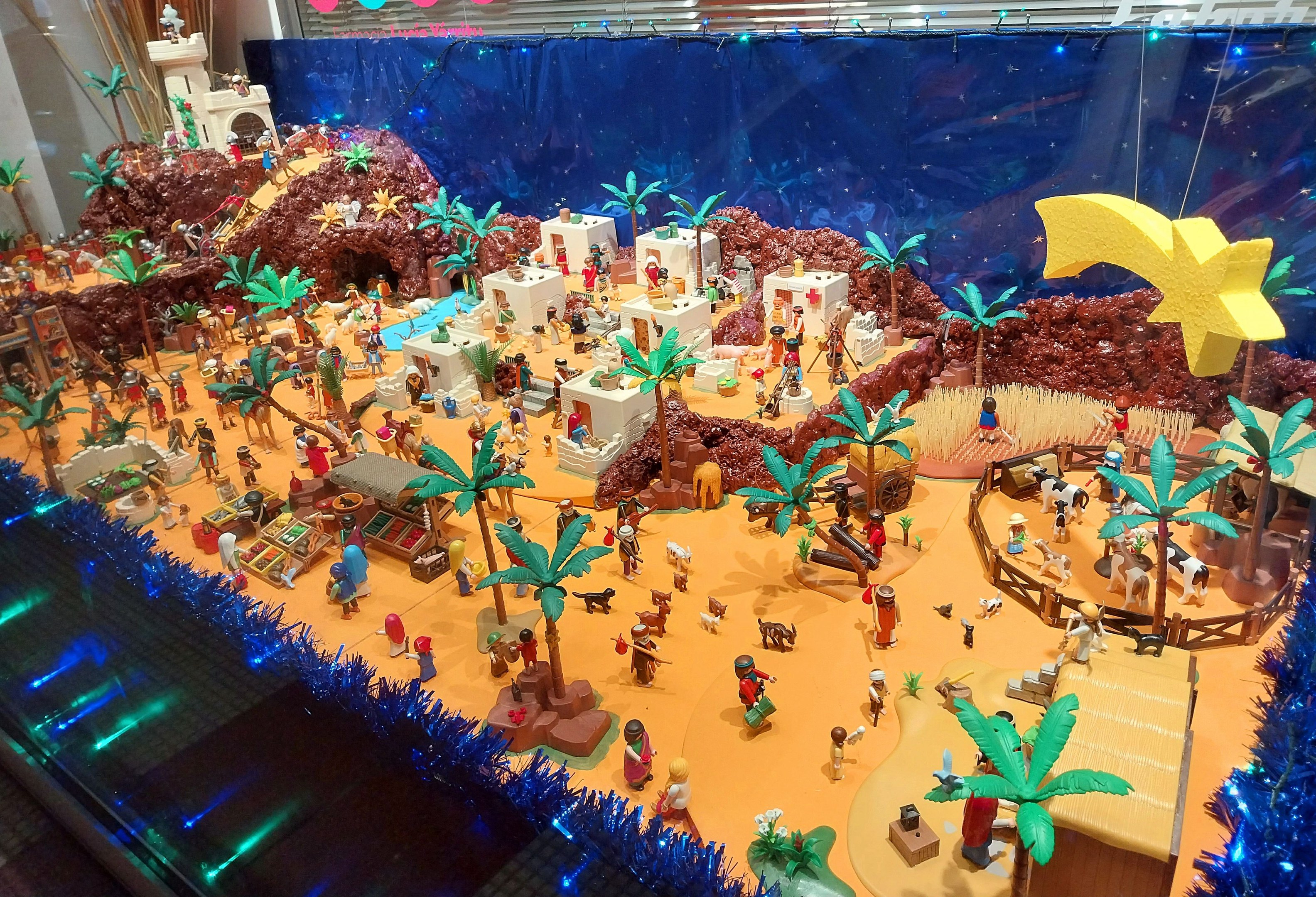 Vitrine voller verschiedener Lego-Steine und -Figuren auf einem Tisch, umgeben von Spielzeugen und dekorativen Elementen, mit beleuchteter Wand im Hintergrund.