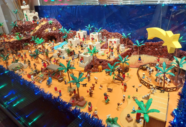 Vitrine voller verschiedener Lego-Steine und -Figuren auf einem Tisch, umgeben von Spielzeugen und dekorativen Elementen, mit beleuchteter Wand im Hintergrund.