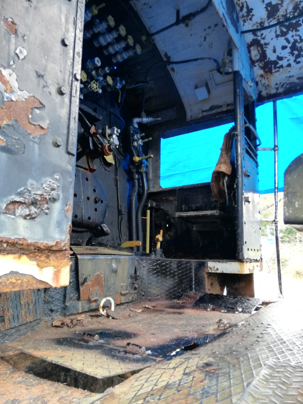 Das Innere einer verrosteten, heruntergekommenen Lkw-Kabine mit sichtbaren Gebrauchsspuren vor dem Hintergrund von Bäumen und einem klaren blauen Himmel.