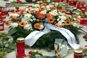 Mahnmal in Berlin mit Blumen und Kerzen vor einer Wand