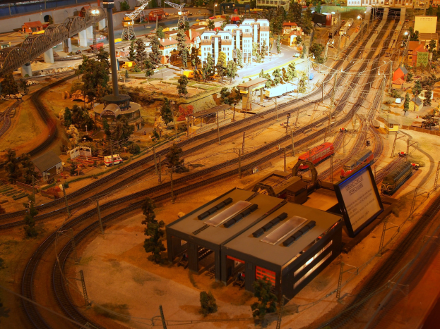 Eine detaillierte Modelleisenbahnausstellung in einem Museum, die Gebäude, Bäume, Eisenbahnschienen, Fahrzeuge, Pfosten, Lichter und Schilder enthält und eine belebte Stadtlandschaft nachahmt.