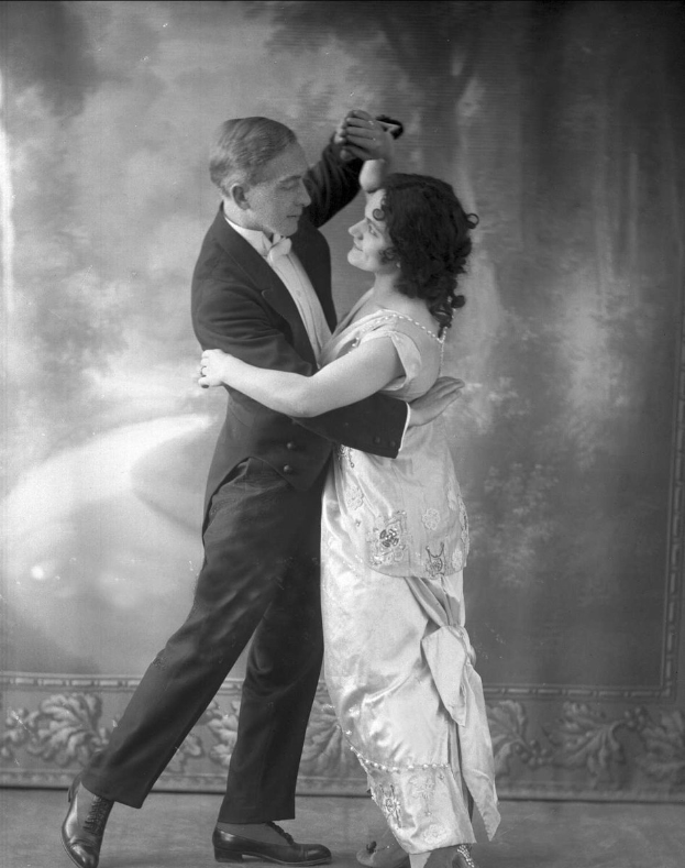 Altes Schwarz-Weiß-Foto eines Mannes in einem Anzug und einer Frau, die Tango tanzen, mit detaillierten Wanddesigns im Hintergrund.