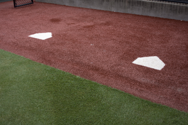 Baseballfeld mit Kunststoffrasen, einer umliegenden Mauer, Home Plate in der Mitte und einer Wand im Hintergrund.