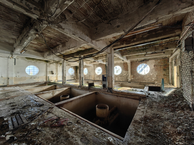 Verlassene Gebäudeinnenseite im Chernobyl-Ausschlussgebiet, das verstreute Trümmer wie Fenster, Säulen, Rohre und Wände mit einer sichtbaren Decke zeigt.