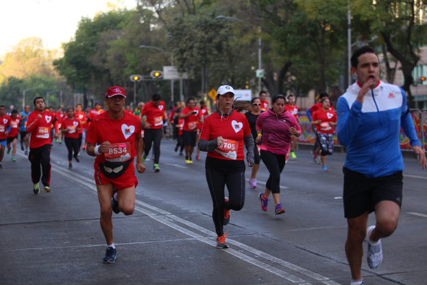 Gruppe von Menschen, die bei einem Marathon auf einer von Bäumen gesäumten Straße mit Laternen, Ampeln, Gebäuden und einem klaren blauen Himmel laufen.