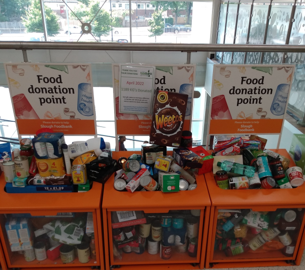 Orange Schübe mit Lebensmittelflaschen, Dosen und Kisten, neben Texttafeln, mit Fahrzeugen, Bäumen, Gebäuden und Himmel durch Glasfenster sichtbar.