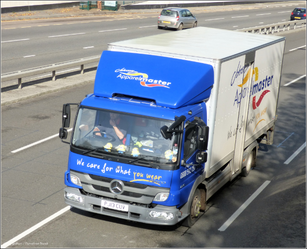 Eine Straße mit wenigen fahrenden Fahrzeugen, einer mittigen Begrenzung und einer Metallkonstruktion oben.