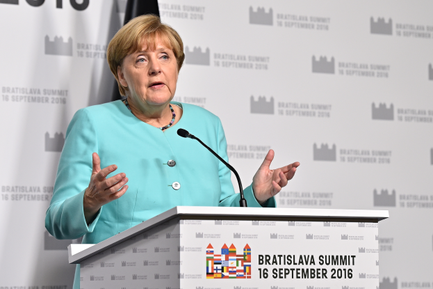 Bundeskanzlerin Angela Merkel hält eine Rede auf dem Bratislava-Gipfel in der Slowakei, vor einem Podium mit zwei Mikrofonen, mit einem Banner und einer Flagge im Hintergrund.