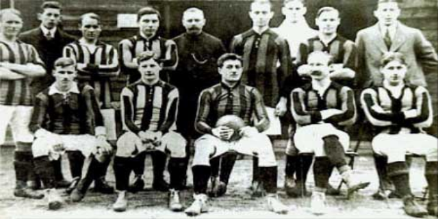 Ein Schwarz-Weiß-Foto einer Fußballmannschaft, mit einigen stehenden und einigen sitzenden Spielern vor einer Wand, mit dem Text 'Ballymena Football Club' unten.