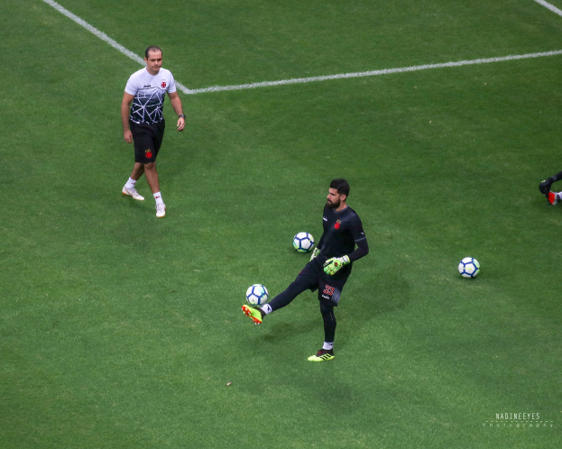 Mann in Sportbekleidung kickt Fußball auf grünem Rasen.