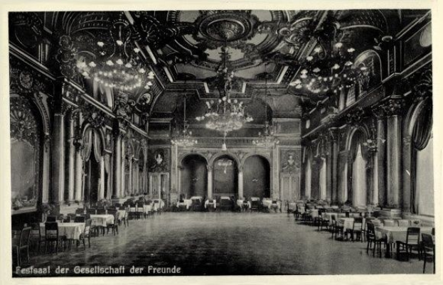 Schwarzes und weißes Foto eines großen Saals mit Tischen, Stühlen, Säulen, Bögen und Deckenleuchtern, beschriftet mit "Festival der Gesellschaft der Freunde, Berlin" unten.